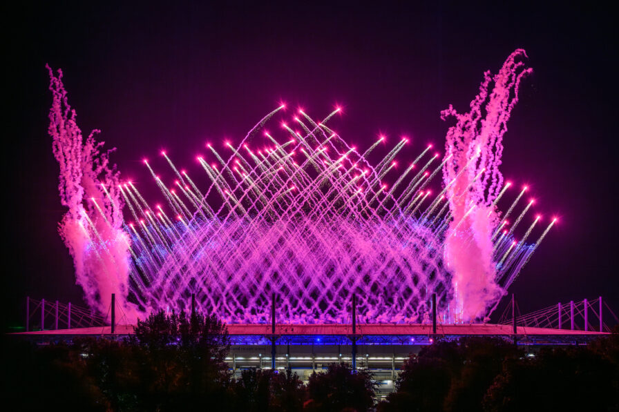 Großflächiges Feuerwerk über dem Stadionhimmel bei Nacht mit goldenen Kometen und Glitzer-Effekten.