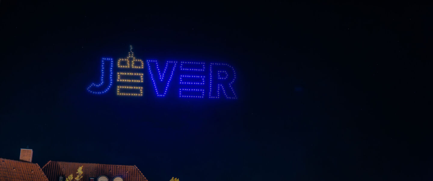 Stadtlogo Jever als leuchtende Drohnenformation am Nachthimmel